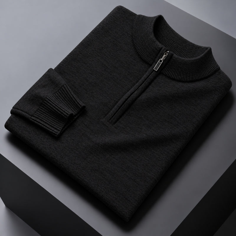 A folded dark charcoal gray knit sweater with a mock neck and a short zipper at the collar, displayed on a dark gray geometric surface.