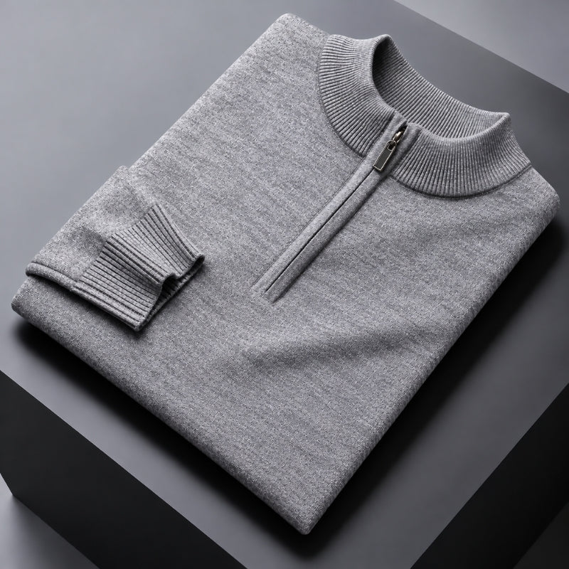A folded light gray knit quarter-zip sweater with a ribbed mock neck and sleeve cuff, displayed on a dark gray geometric surface.