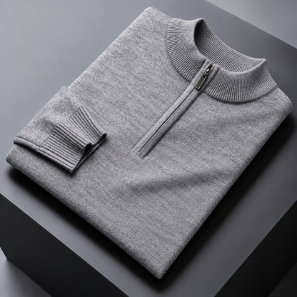A folded light gray knit quarter-zip sweater with a ribbed mock neck and sleeve cuff, displayed on a dark gray geometric surface.