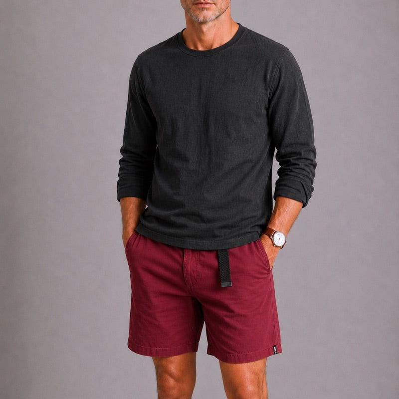 Man wearing a black long-sleeve shirt and red shorts against a gray background