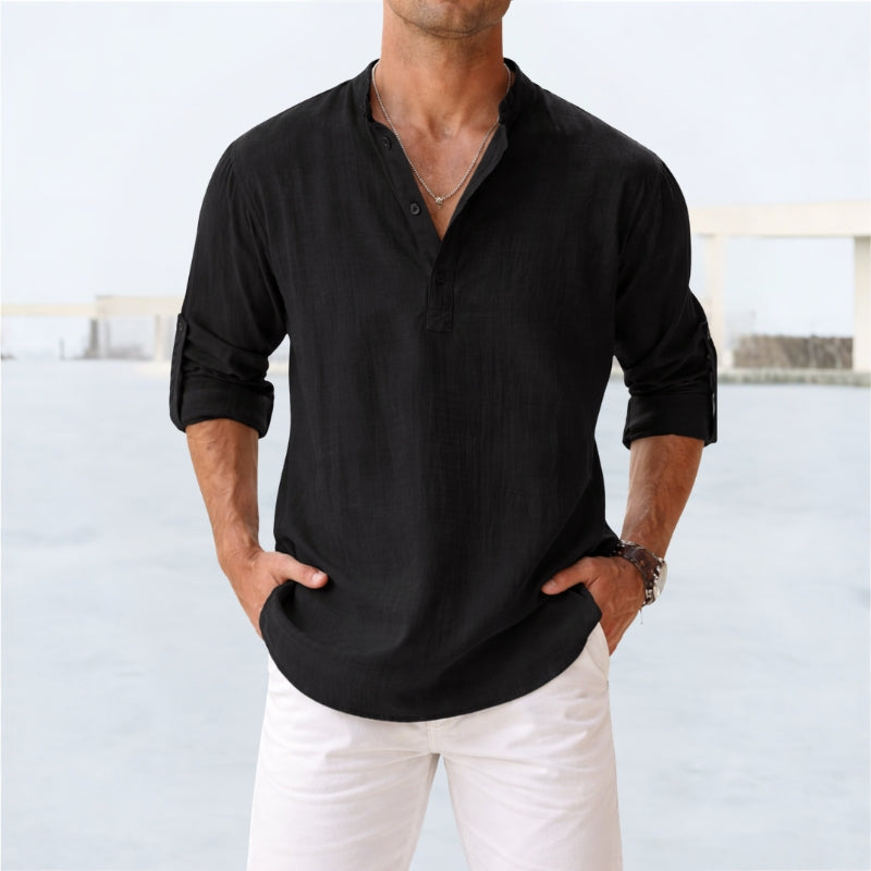 Man wearing a black long-sleeve shirt and white pants against a light background