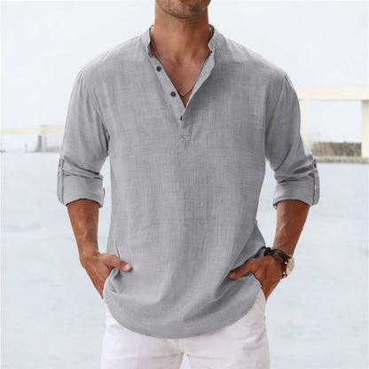 Man wearing a gray long-sleeve shirt with rolled-up sleeves and white pants against a light background