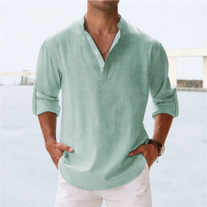 Man wearing a light green shirt with rolled-up sleeves against a blurred outdoor background