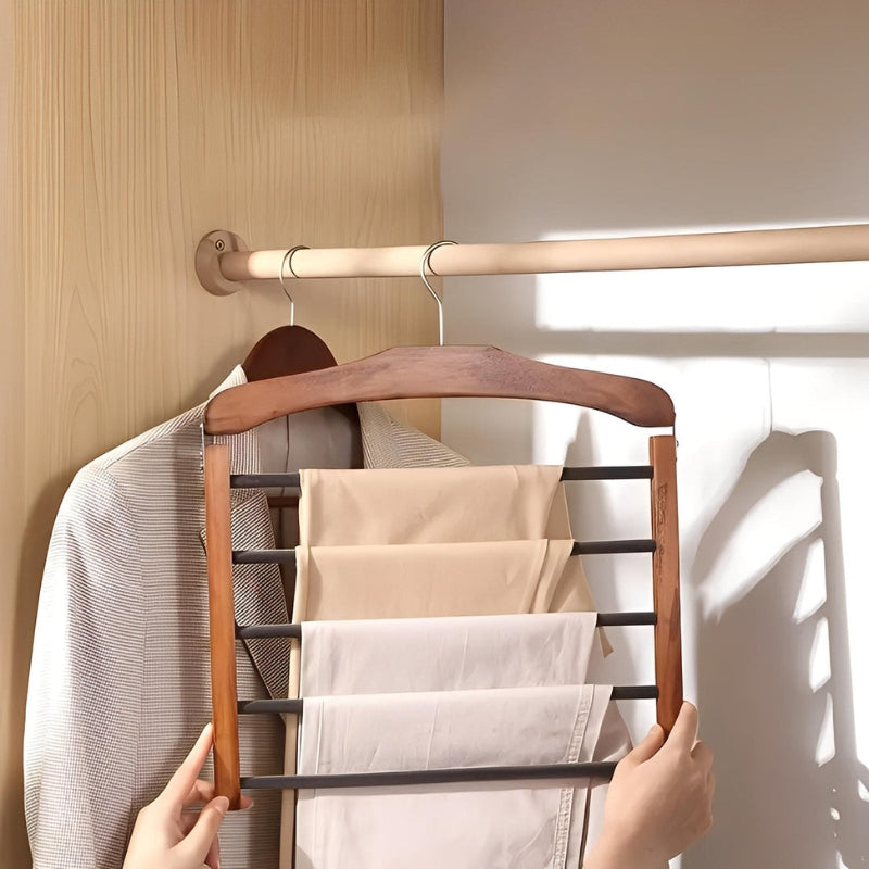 Wooden hanger with a multi-tiered rack holding folded clothes against a neutral wall.