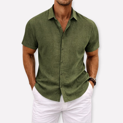 Man wearing a green short-sleeve shirt and white pants against a light gray background
