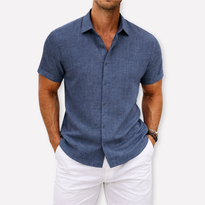 Man wearing a blue short-sleeve shirt and white pants against a light background