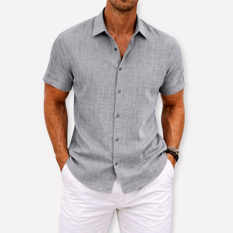 Man wearing a gray short-sleeve button-up shirt and white pants on a light background