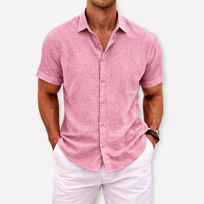 Man wearing a pink short-sleeve shirt and white pants against a white background