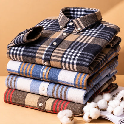 A stack of folded plaid button-up shirts in various colors and patterns, including navy, beige, blue, and red, styled with cotton bolls on a warm beige background.