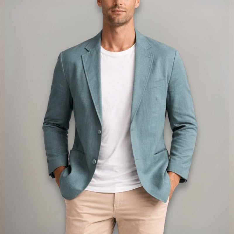 Man wearing a light blue blazer over a white shirt and beige pants against a gray background