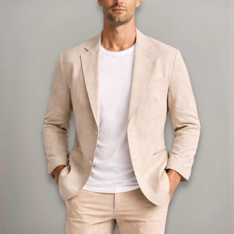 Man wearing a beige blazer over a white shirt and beige pants against a gray background