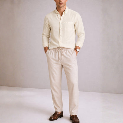 Man wearing a beige shirt and pants with brown shoes on a plain background