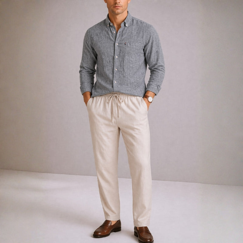 Man wearing a gray button-up shirt, beige pants, and brown shoes against a plain background