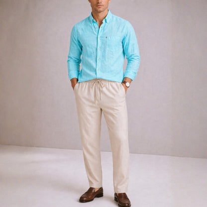 Man wearing a turquoise shirt and beige pants against a plain background
