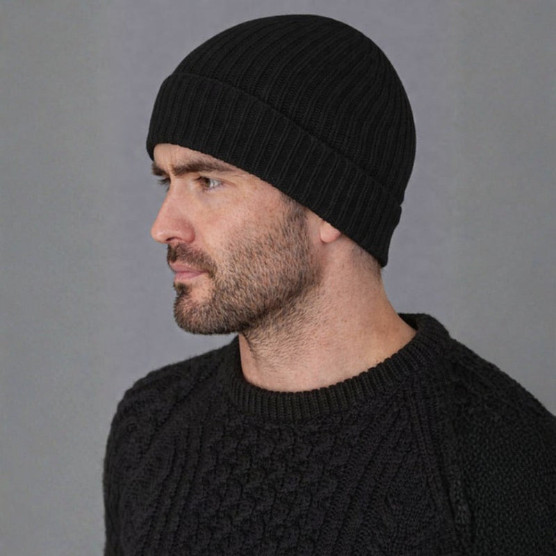 Man wearing a black knit beanie and sweater against a gray background