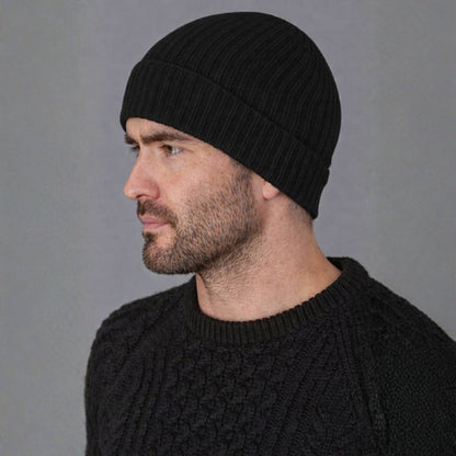 Man wearing a black knit beanie and sweater against a gray background
