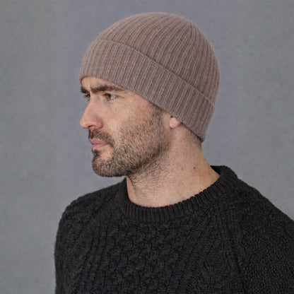 Man wearing a brown beanie and black sweater against a gray background