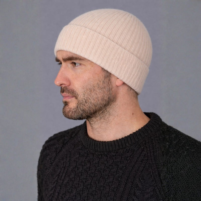 Man wearing a beige beanie and black sweater against a gray background