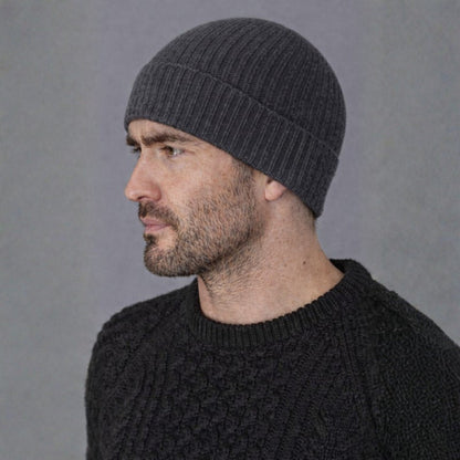 Man wearing a dark gray knit beanie and black sweater against a gray background