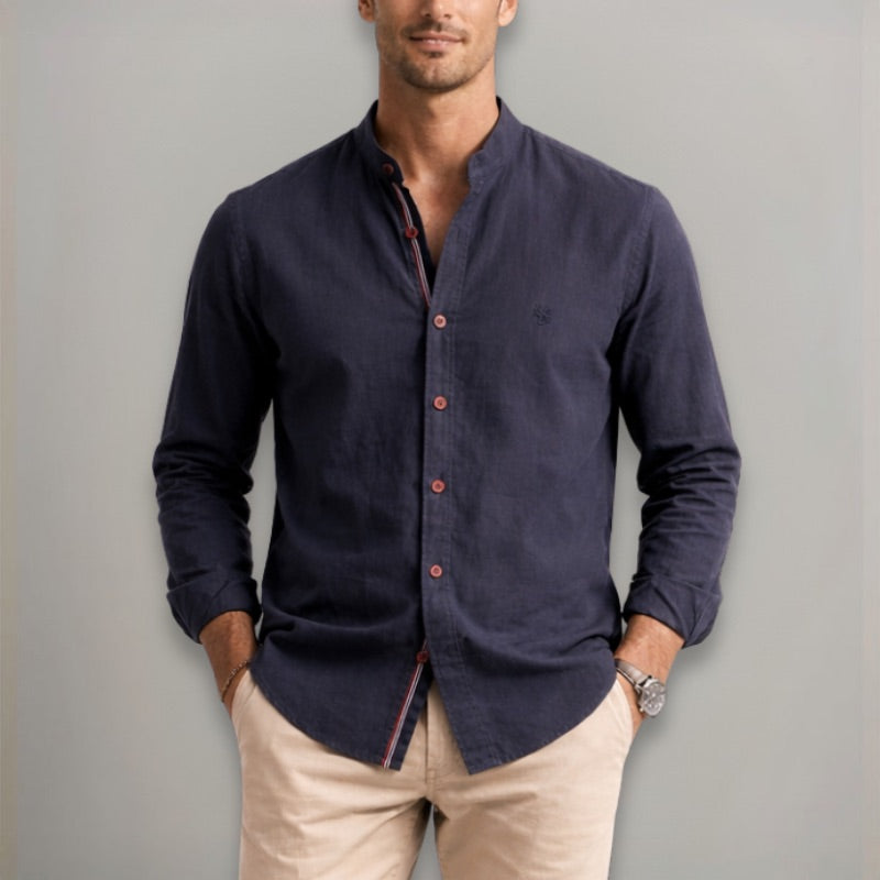 Man wearing a navy button-up shirt and beige pants against a gray background