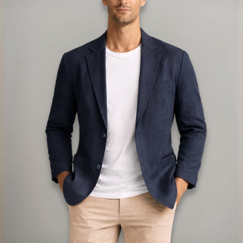 Man wearing a navy blazer over a white shirt and beige pants against a gray background
