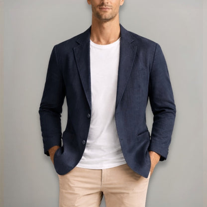 Man wearing a navy blazer over a white shirt and beige pants against a gray background