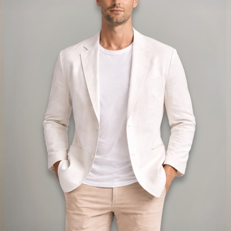 Man wearing a light-colored blazer over a white shirt and beige pants against a gray background