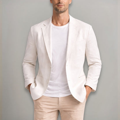Man wearing a light-colored blazer over a white shirt and beige pants against a gray background
