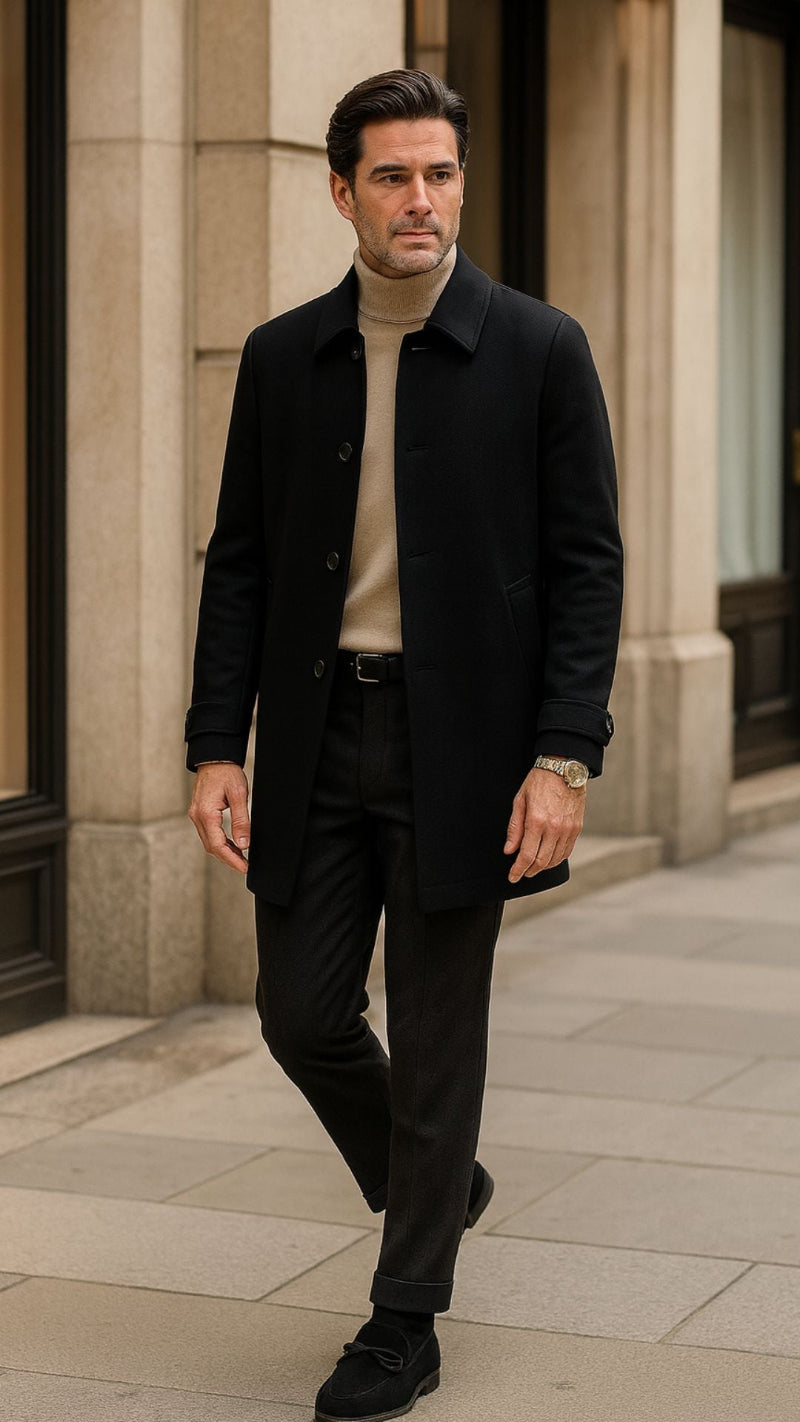 Black Giacomo Urban Coat from Polumi layered over a beige turtleneck with dark trousers. Premium elegant menswear for confident cooler-season style in the city.