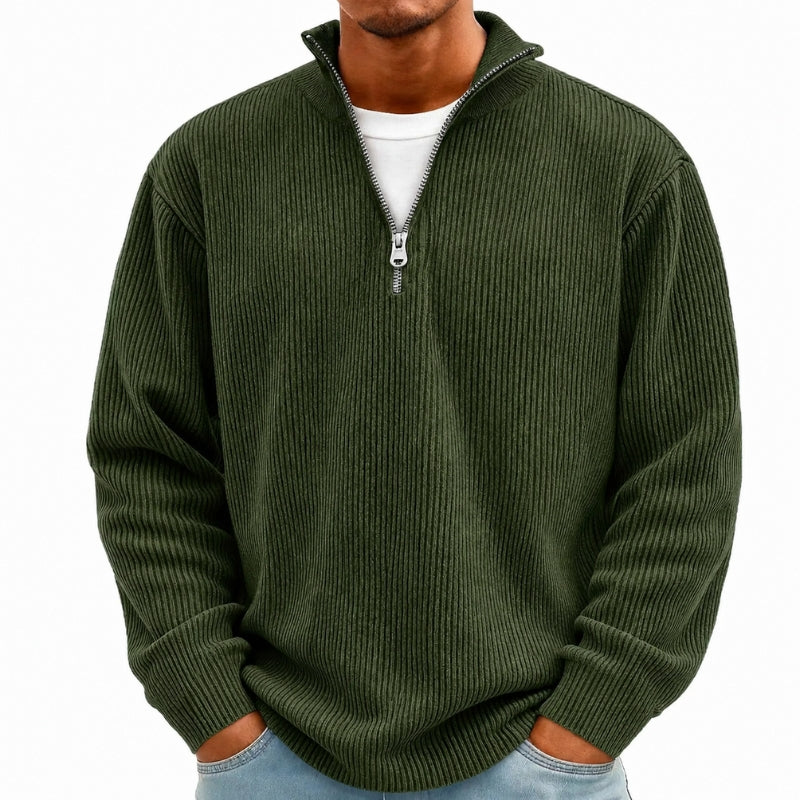 A man wearing a dark olive green ribbed knit quarter-zip pullover sweater over a white t-shirt and light blue jeans, shown from the neck down against a plain white background.