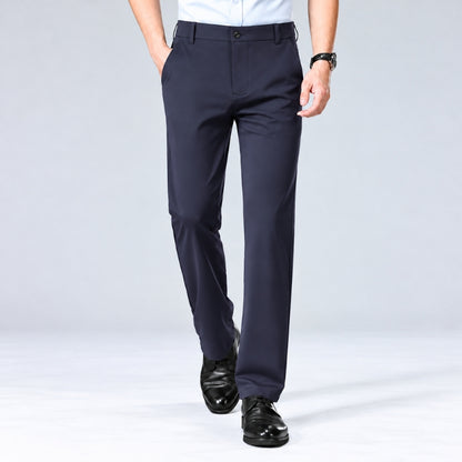 A person wearing dark navy dress pants with a white shirt and black dress shoes, shown from the waist down against a light gray studio background.