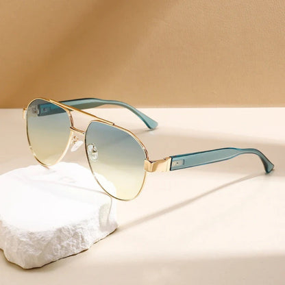 Luigi Italian Aviators Sunglasses in slate teal with gradient blue-yellow lenses and gold metal frame, displayed on beige background.