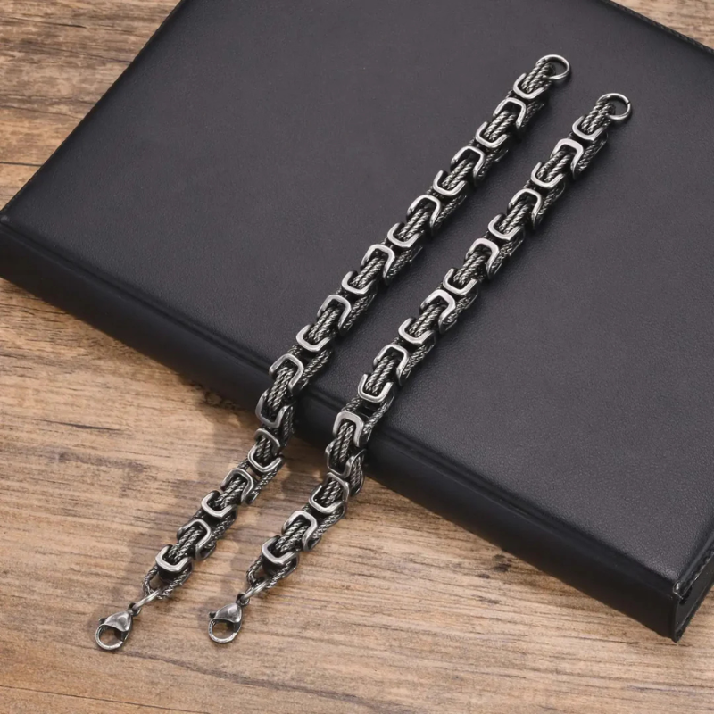 Pair of men’s rope chain bracelets in gunmetal finish with square links, bold stainless steel jewelry on wooden surface.