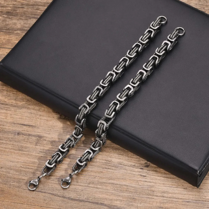 Pair of men’s rope chain bracelets in gunmetal finish with square links, bold stainless steel jewelry on wooden surface.