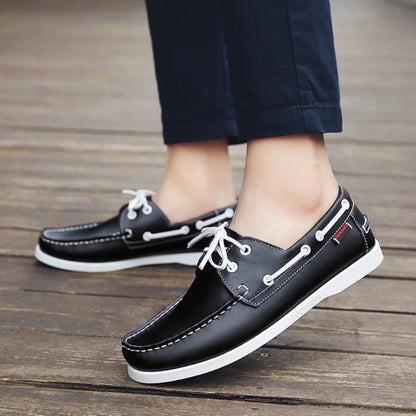 Black men’s leather boat shoes with nautical laces worn with navy pants, classic casual footwear for smart summer looks.