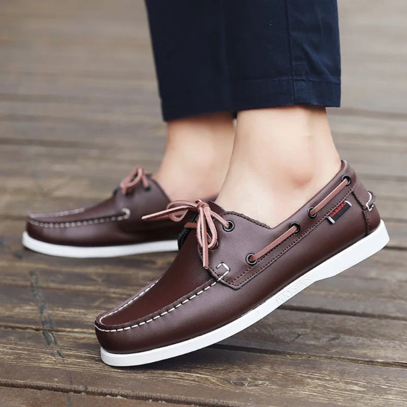 Brown men’s leather boat shoes with white sole and stitching worn with trousers, versatile moccasins for casual or travel outfits.