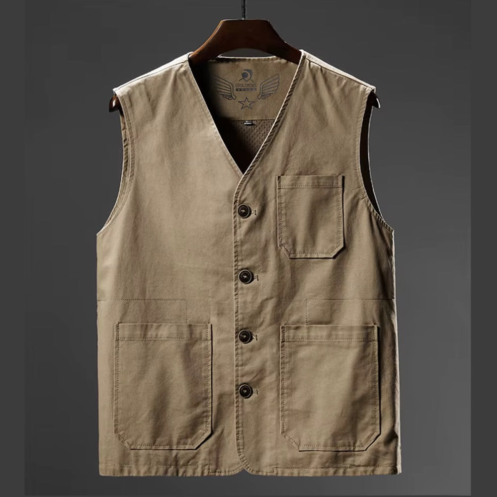 A sleeveless utility vest in a warm khaki-beige color, hanging on a dark wooden hanger against a dark gray gradient background. The vest features a V-neck, a button-up front, a chest pocket, and two large front patch pockets.