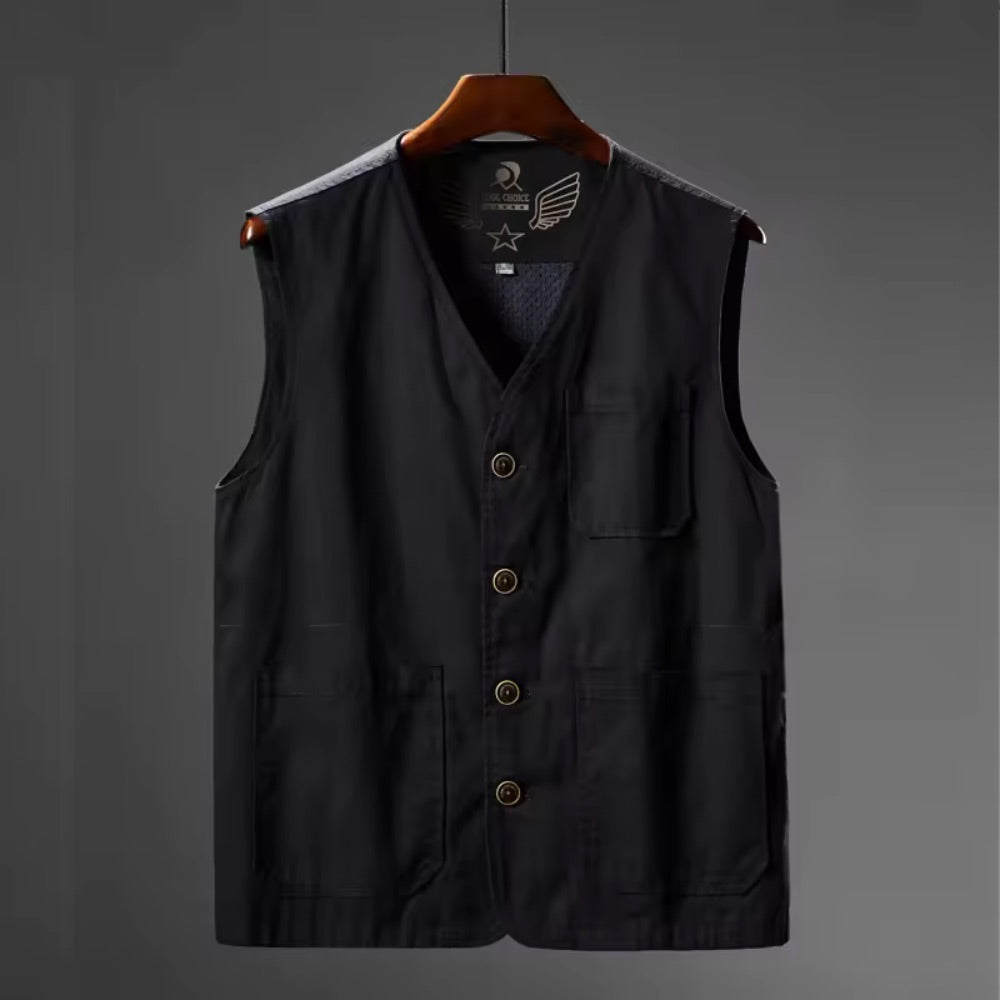 A black utility vest with a V-neck, button closure, and four front pockets, hanging on a wooden hanger against a dark gray background.