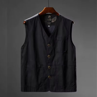 A black utility vest with a V-neck, button closure, and four front pockets, hanging on a wooden hanger against a dark gray background.