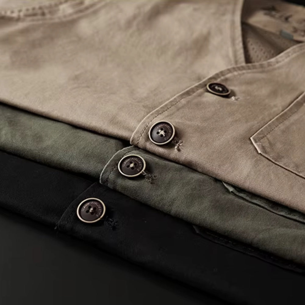 Close-up of folded button-front shirts in beige, olive green, and black, showing the fabric texture and dark buttons.