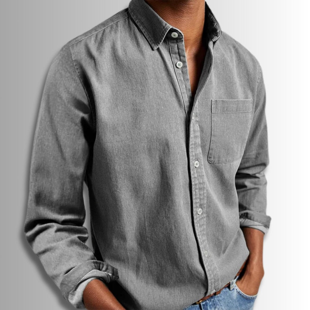 Person wearing a gray button-up shirt with rolled-up sleeves on a plain background